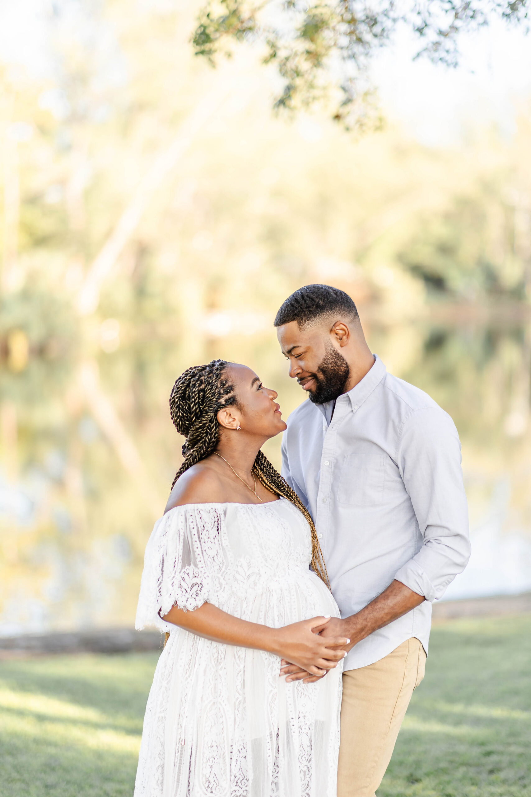 A happy pregnant couple smiles at each other with hands on the bump by a Miami lake