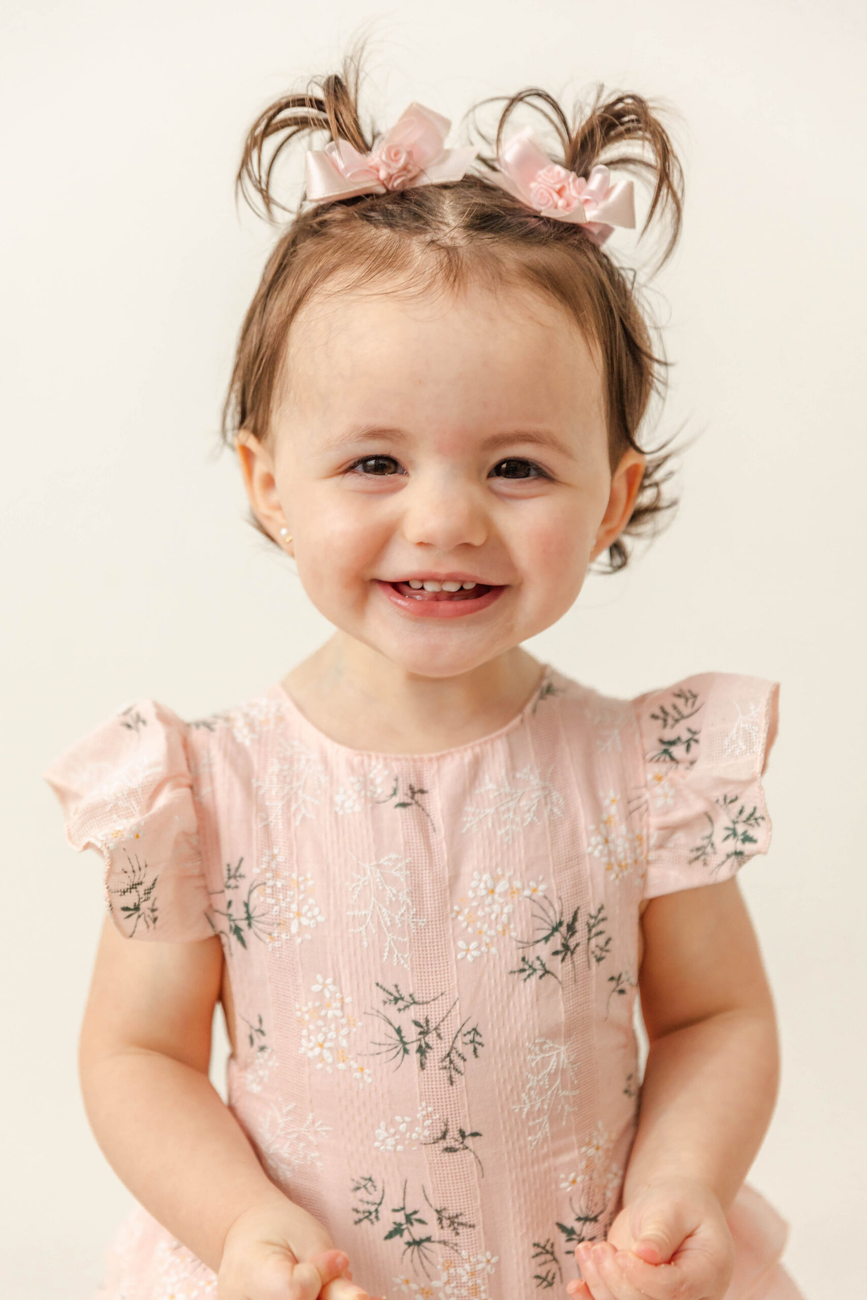 A closeup of a giggling toddler girl in a pink dress and matching pigtail bows