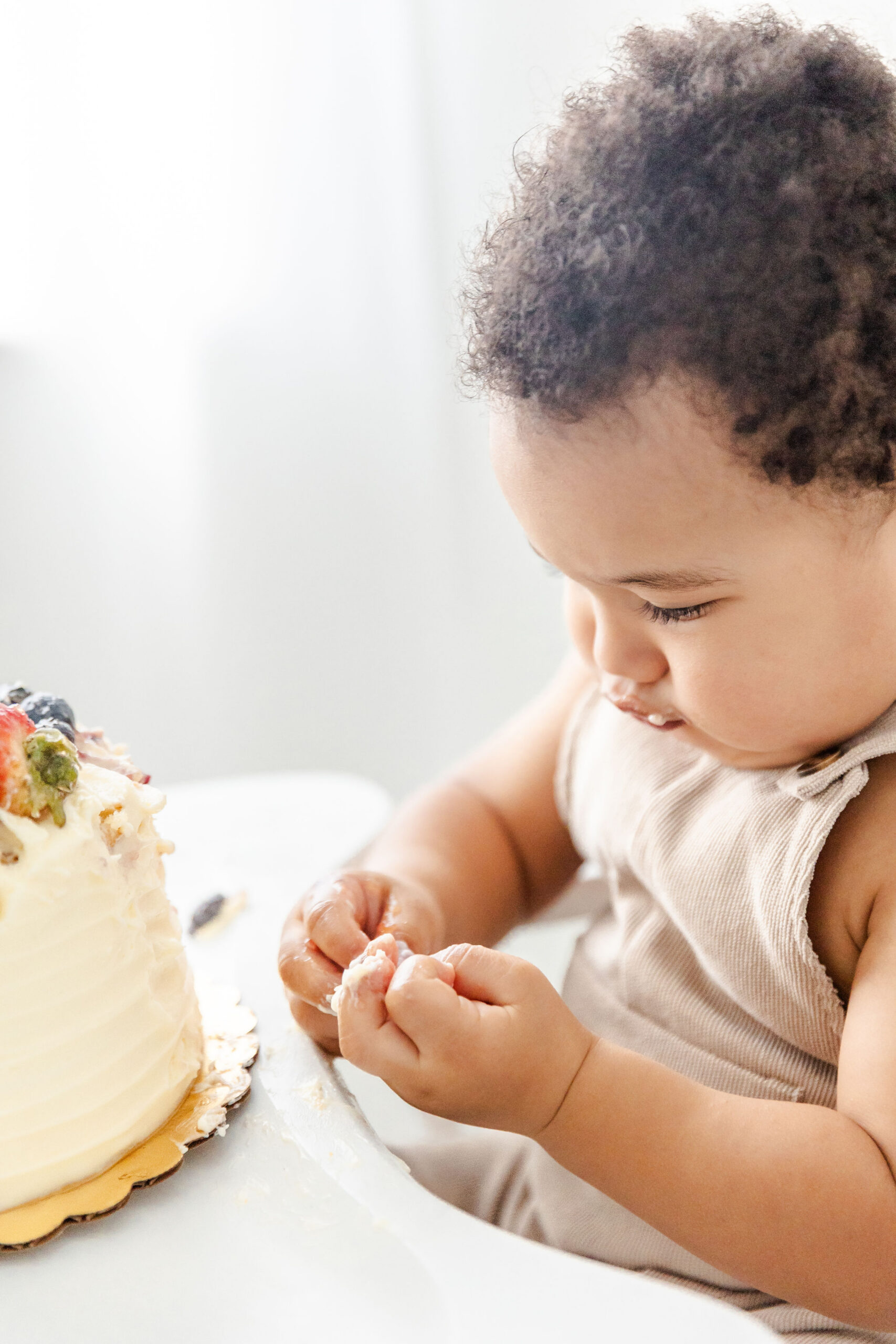 A toddler sits in a high chair examining the cake icing covering his hands