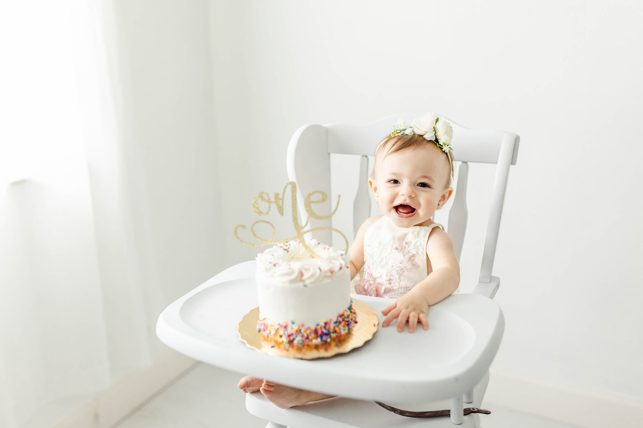 A happy baby girl in a high chair for her birthday cake smash after visiting the shoppe miami